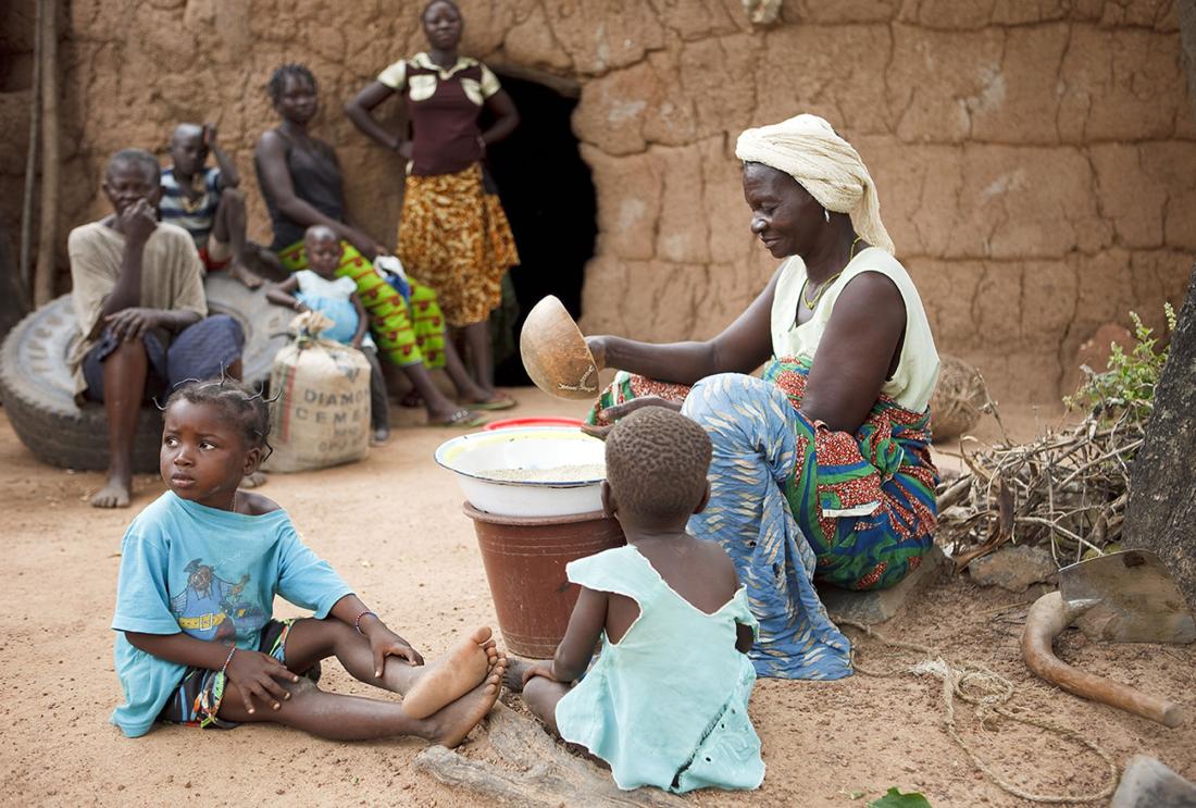 Woman sorts grain while caring for children in Burkina Faso.