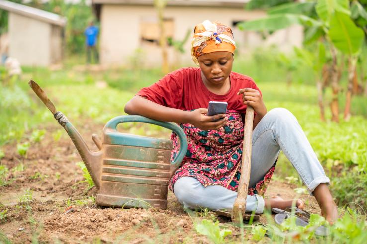 Woman sitting on the ground with farming tools on smart phone
