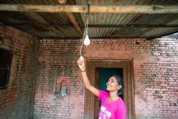 A smiling woman pulls a cord, turning on a lightbulb. 